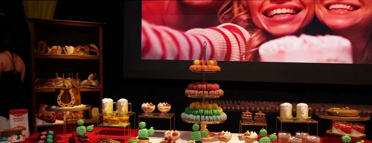 Mesa de exposição da Diniz Foods cheia de doces e bolos num evento do setor